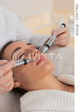 Caucasian young woman gets lips zone facial therapy with modern device by cosmetologist in clinic Caucasian young woman gets lips zone facial therapy with modern device by cosmetologist in clinic 125677462