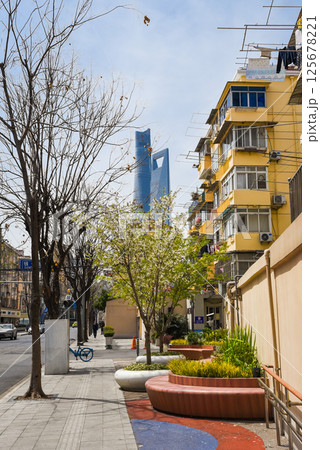 Shanghai, China - 1 April 2025: Pudong street with spring blossoms, colorful benches, and view of Shanghai Tower and World Financial Center in background. 125678221