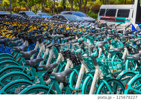 Shanghai, China - 1 April 2025: Blue rental bikes parked in urban area. Empty parking lot with cars visible. No people. Clear day Shanghai, China - 1 April 2025: Blue rental bikes parked in urban area. Empty parking lot with cars visible. No people. Clear day 125678227