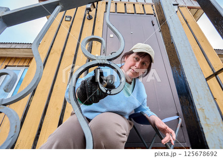 Painting decorative porch railing at entrance of country house, white woman around 50 years old is using paintbrush. 125678692