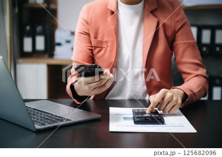 Businessman hands working with finances about cost and calculator and laptop with tablet, smartphone at office in morning light Businessman hands working with finances about cost and calculator and laptop with tablet, smartphone at office in morning light 125682096