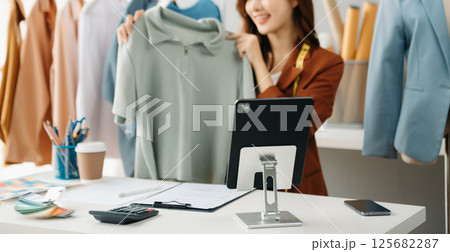 Fashion blogger concept, Young Asian women selling clothes on video streaming.Startup small business SME, using smartphone or tablet taking receive 125682287