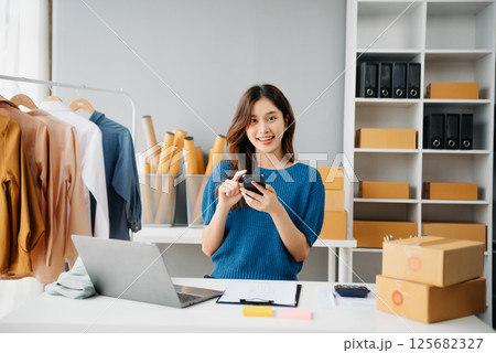 Asian lady blogger showing clothes in front of the camera to recording vlog video live streaming at her shop. Online Shopping 125682327