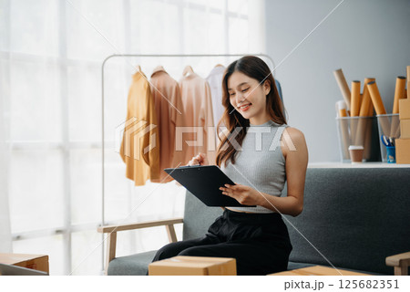 Asian lady blogger showing clothes in front of the camera to recording vlog video live streaming at her shop. Online Shopping 125682351