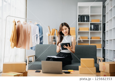 Asian lady blogger showing clothes in front of the camera to recording vlog video live streaming at her shop. Online Shopping 125682353