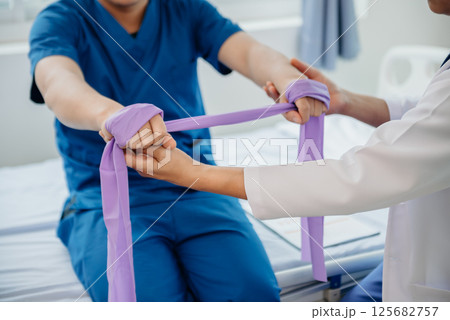 Physiotherapist Helping Patient While Stretching His Leg in bed in clinic Physiotherapist Helping Patient While Stretching His Leg in bed in clinic 125682757