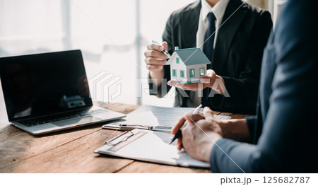 Real estate broker agent presenting and consult to customer to decision making sign insurance form agreement, home model, concerning mortgage loan offer in office Real estate broker agent presenting and consult to customer to decision making sign insurance form agreement, home model, concerning mortgage loan offer in office 125682787