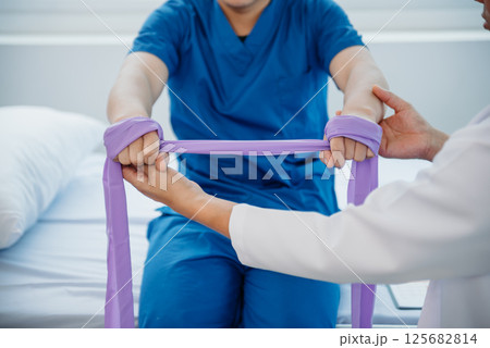 Physiotherapist Helping Patient While Stretching His Leg in bed in clinic Physiotherapist Helping Patient While Stretching His Leg in bed in clinic 125682814