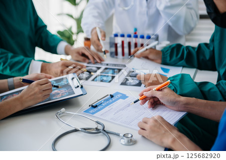 Medical team having a meeting with doctors in white lab coats and surgical scrubs seated at a table discussing a patients working online using computers in the medical industry 125682920