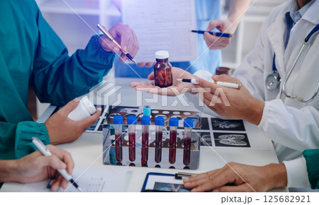 Medical team having a meeting with doctors in white lab coats and surgical scrubs seated at a table discussing a patients working online using computers in the medical industry 125682921
