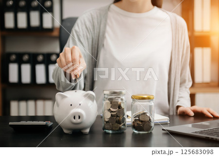 Woman hand holding coin with pig piggy bank. Saving and financial accounts concept 125683098