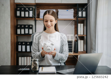 Caucasian Women are putting coins in a piggy bank for a business that grows for profit and saving money for the future. Caucasian Women are putting coins in a piggy bank for a business that grows for profit and saving money for the future. 125683242