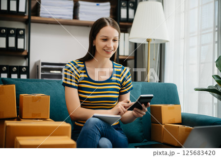 Caucasian young woman SME working using smartphone or tablet taking receive and checking online purchase shopping order to freelance online concept. 125683420