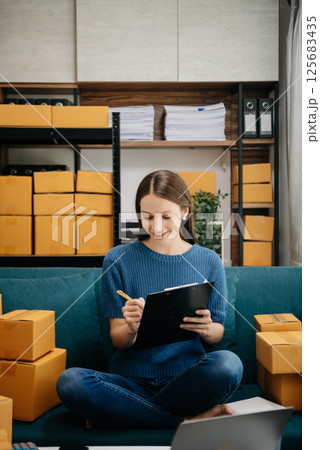 Caucasian young woman SME working using smartphone or tablet taking receive and checking online purchase shopping order to freelance online concept. 125683435