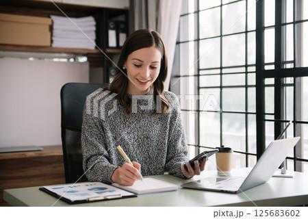 Confident business expert attractive smiling young woman typing laptop ang holding digital tablet on desk in creative office. Confident business expert attractive smiling young woman typing laptop ang holding digital tablet on desk in creative office. 125683602