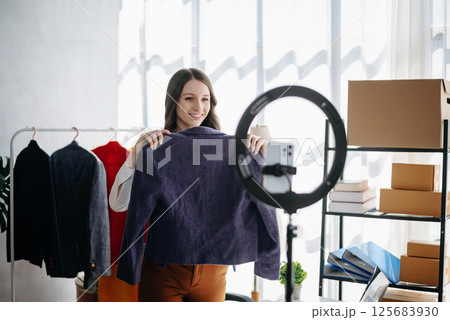 Beautiful Asian lady blogger showing clothes in front of the camera to recording vlog video live streaming at her shop. Online Shopping Beautiful Asian lady blogger showing clothes in front of the camera to recording vlog video live streaming at her shop. Online Shopping 125683930