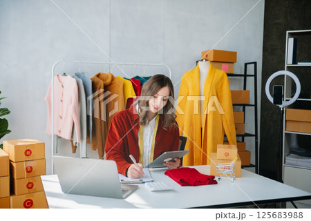 Fashion designer woman talking smart phone and using laptop with digital tablet computer in modern studio Fashion designer woman talking smart phone and using laptop with digital tablet computer in modern studio 125683988