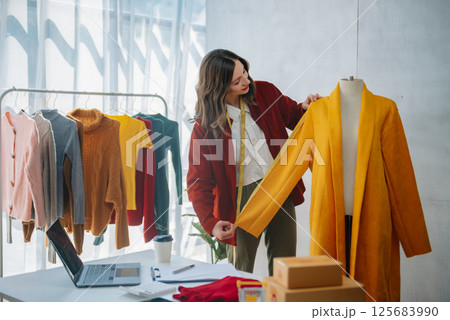 Calm curly brunette dark skinned woman on desk in office of fashion designer and holds tablet and smartphone. Calm curly brunette dark skinned woman on desk in office of fashion designer and holds tablet and smartphone. 125683990