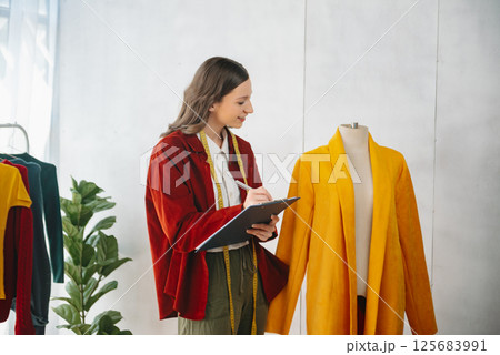 Calm curly brunette dark skinned woman on desk in office of fashion designer and holds tablet and smartphone. Calm curly brunette dark skinned woman on desk in office of fashion designer and holds tablet and smartphone. 125683991
