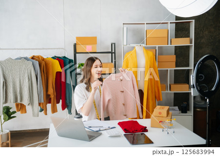 Beautiful lady blogger showing clothes in front of the camera to recording vlog video live streaming at her shop. Online Shopping Cart notion. 125683994