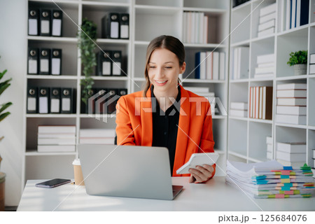 Beautiful woman using laptop and tablet while sitting at her working place. Concentrated at work. Beautiful woman using laptop and tablet while sitting at her working place. Concentrated at work. 125684076