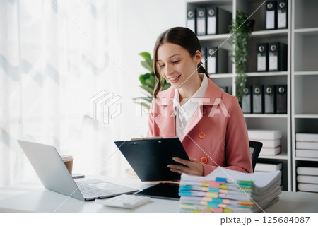 Beautiful woman using laptop and tablet while sitting at her working place. Concentrated at work. 125684087