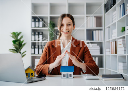 Female real estate agent is use hands to protect red roof for the concept of real estate investment about house trading, purchase at desk in office Female real estate agent is use hands to protect red roof for the concept of real estate investment about house trading, purchase at desk in office 125684171