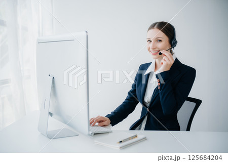 Serious call center operator in wireless headset talking with customer, woman in headphones with microphone consulting client on phone in customer support service in business center Serious call center operator in wireless headset talking with customer, woman in headphones with microphone consulting client on phone in customer support service in business center 125684204
