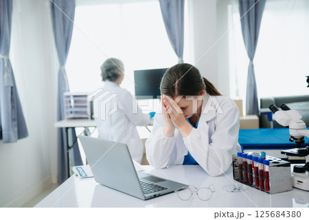 Confident young Caucasian female doctor in white medical uniform sit at desk working on computer. Smiling use laptop write in medical journal Confident young Caucasian female doctor in white medical uniform sit at desk working on computer. Smiling use laptop write in medical journal 125684380