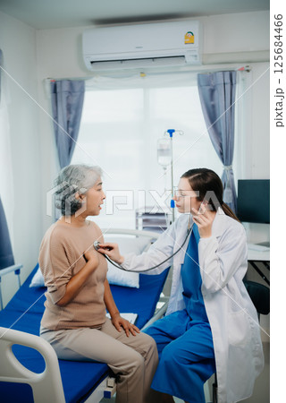 Doctor in white suit take notes while discussing and Asian elderly, woman patient who lying on bed with receiving saline solution in hospital or clinic. Doctor in white suit take notes while discussing and Asian elderly, woman patient who lying on bed with receiving saline solution in hospital or clinic. 125684466