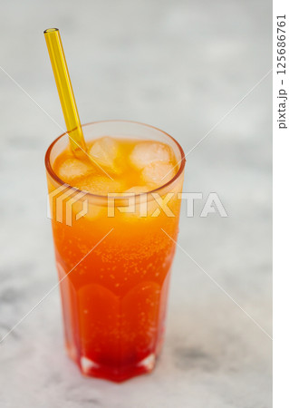 Refreshing Orange Carbonated Drink with Ice Cubes in Tall Glass on Gray Surface, Trendy Dirty Soda Concept 125686761