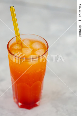 Refreshing Orange Carbonated Drink with Ice Cubes in Tall Glass on Gray Surface, Trendy Dirty Soda Concept 125686763