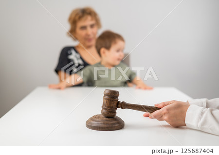 A judge hits a gavel against the backdrop of an elderly woman holding a child. A judge hits a gavel against the backdrop of an elderly woman holding a child. 125687404