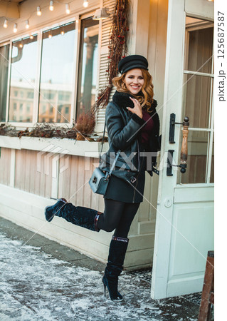 Smiling pretty brunette woman in black leather jacket and high heels with blue handbag standing  125687587