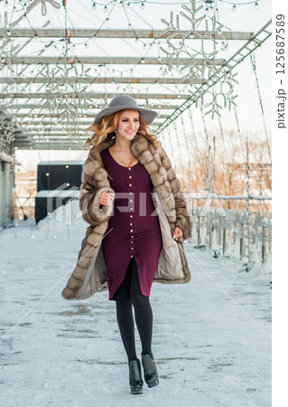 Beautiful woman walking out on city street background in cold outdoor wearing hat and fur coat 125687589