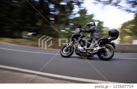 Driver riding motorcycle on empty asphalt road, blurred motiion, spring mountains 125687754