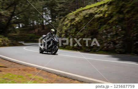 Driver riding motorcycle on empty asphalt road, spring mountains 125687759