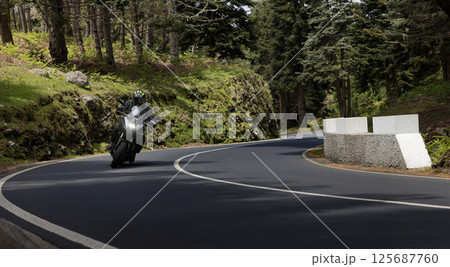 Driver riding motorcycle on empty asphalt road, spring mountains 125687760
