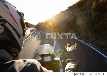 Driver riding motorcycle on empty asphalt road, handlebars view , spring mountains 125687761