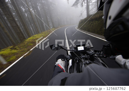 Driver riding motorcycle on empty road , foggy rainforest, handlebars view Driver riding motorcycle on empty road , foggy rainforest, handlebars view 125687762