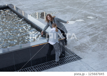 Positive woman and young girl child walking along the streets of the city. Childhood, happiness 125687845