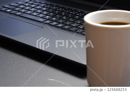 淹れたての美味しいコーヒーを飲みながら、ノートパソコンでデスクワークをしているイメージ写真 淹れたての美味しいコーヒーを飲みながら、ノートパソコンでデスクワークをしているイメージ写真 125688253