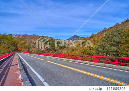 秋の山梨県北杜市の川俣川渓谷にかかる赤い橋(東沢大橋)と八ヶ岳 125689203