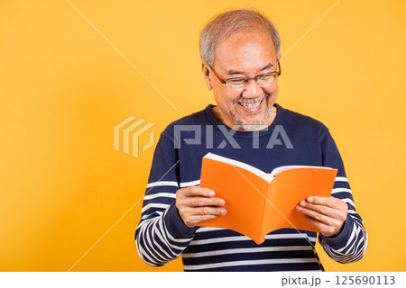 Portrait smiling Asian old man wearing glasses reading a book studio shot isolated yellow background, happy elderly man enjoying interesting story, time to relaxation Portrait smiling Asian old man wearing glasses reading a book studio shot isolated yellow background, happy elderly man enjoying interesting story, time to relaxation 125690113