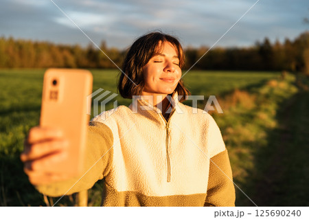 Young woman enjoying golden hour in nature, blending influencer lifestyle with outdoor well-being and digital mindfulness 125690240