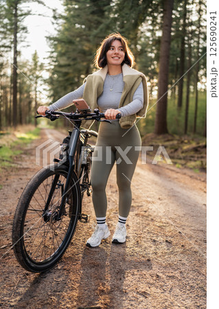 Sporty woman rides forest path on holiday, channeling cycling passion, tranquil travel, and sunny-season wellness 125690241