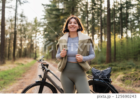 Young woman biking under tall trees, linking mindful movement, seasonal escape, and sport-infused travel 125690243