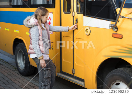Cute girl child school student opens the door of a school bus 125690289