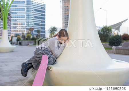 Tired young girl child with skateboard resting outdoors Tired young girl child with skateboard resting outdoors 125690298