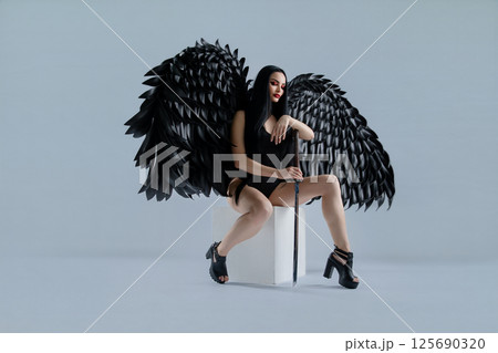 Woman in lingerie with striking black wings poses confidently in studio setting 125690320
